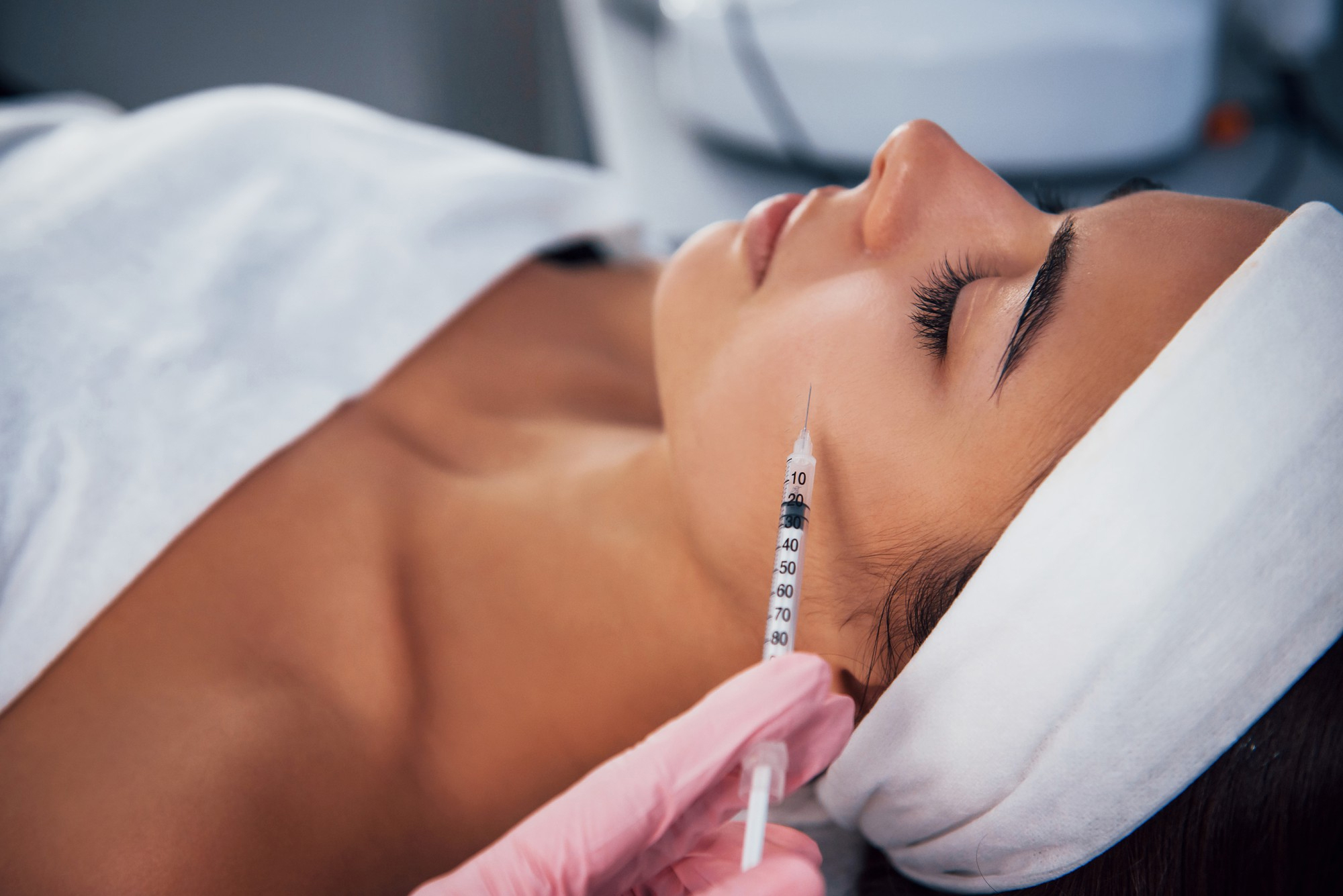 Mujer recibiendo tratamiento estético con inyecciones en la cara, enfocándose en la zona de las mejillas, en un entorno de clínica estética.