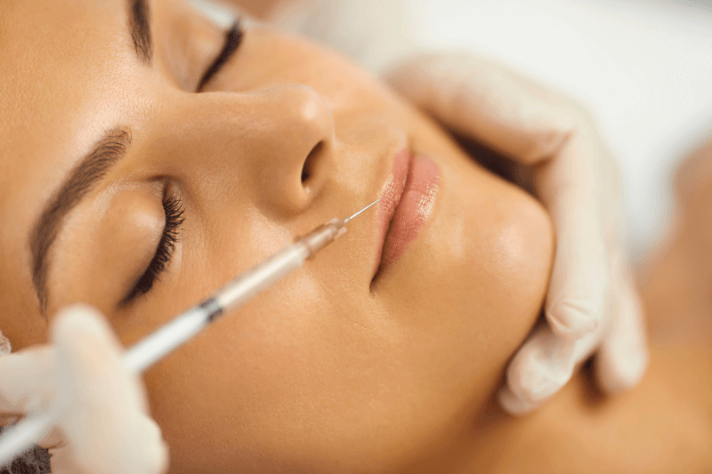 Mujer recibiendo un tratamiento estético de labios con inyección, mostrando atención y cuidado en un ambiente de clínica de belleza.